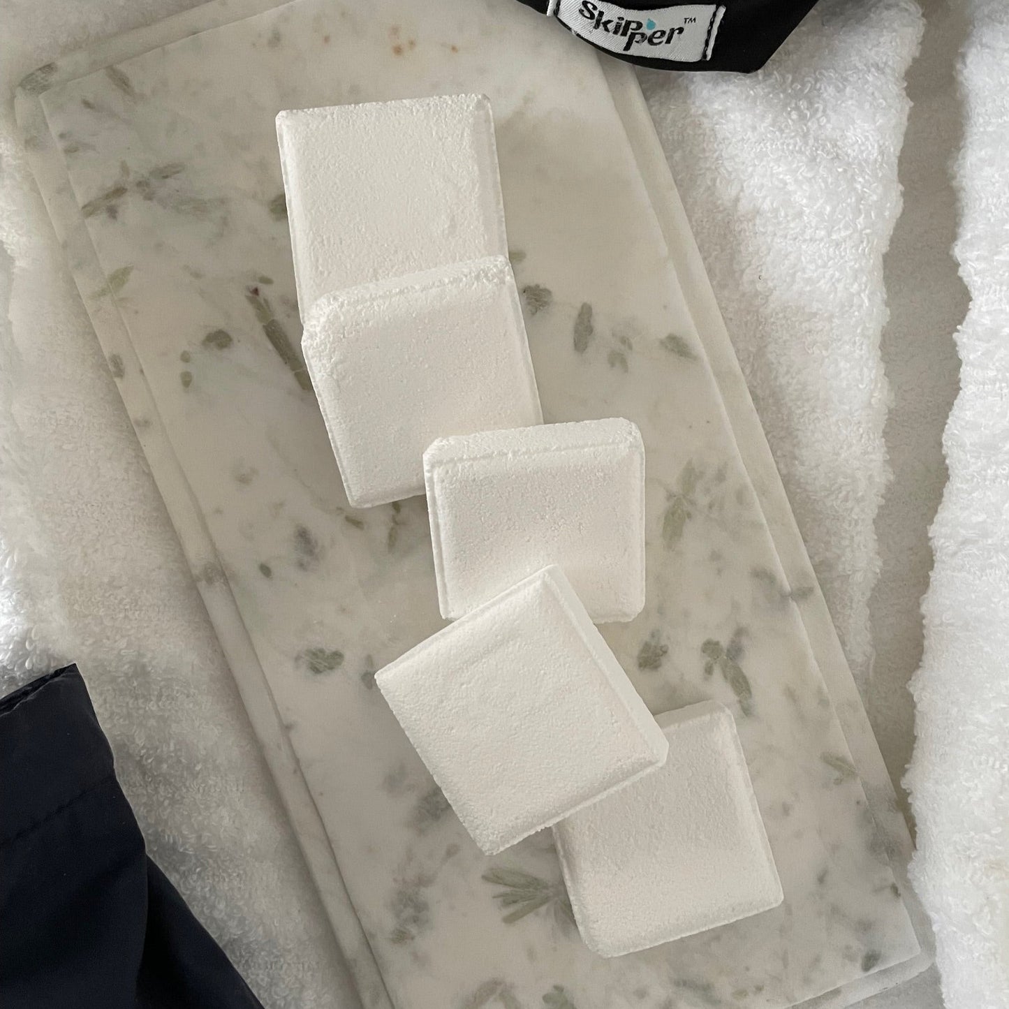 Skipper Shower Steamers on marble with towel texture and shower caps in background