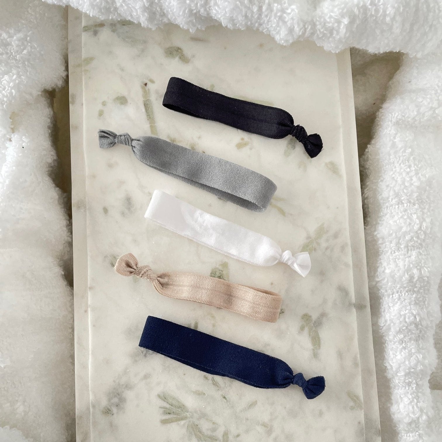 Hair ties on a marble background. Colours are black, grey, white, beige, and navy.