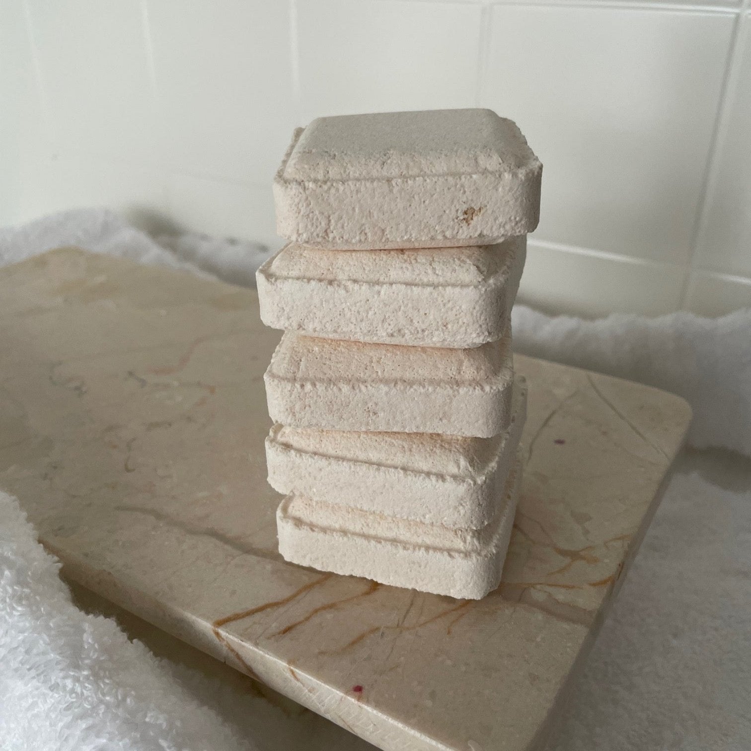 Skipper Shower Steamers stacked on marble with towel texture and tiles in background.